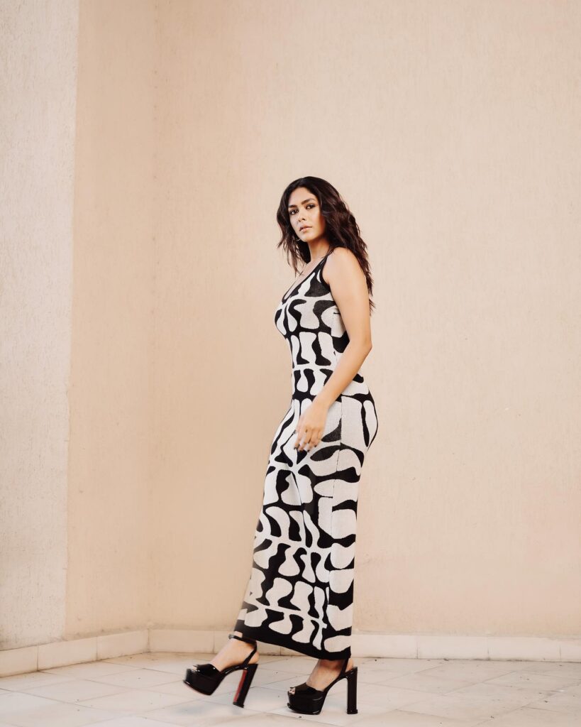 A woman in a black and white dress posing in front of a wall.