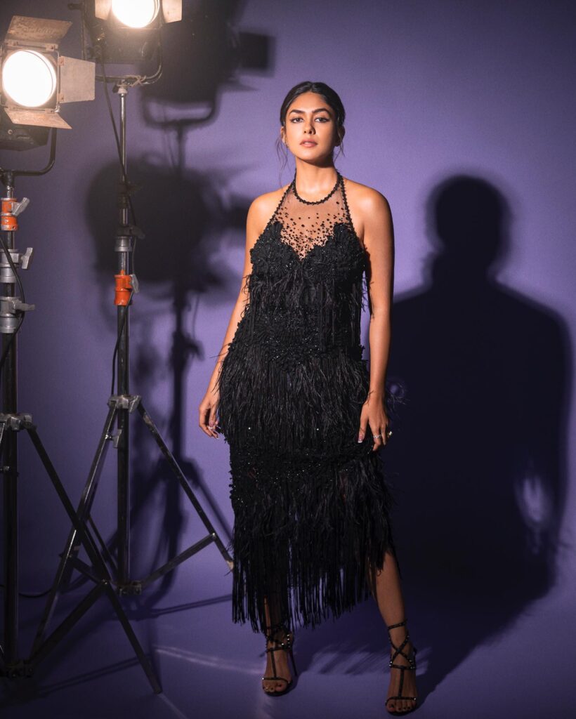 A woman in a black fringe dress posing in front of a camera.